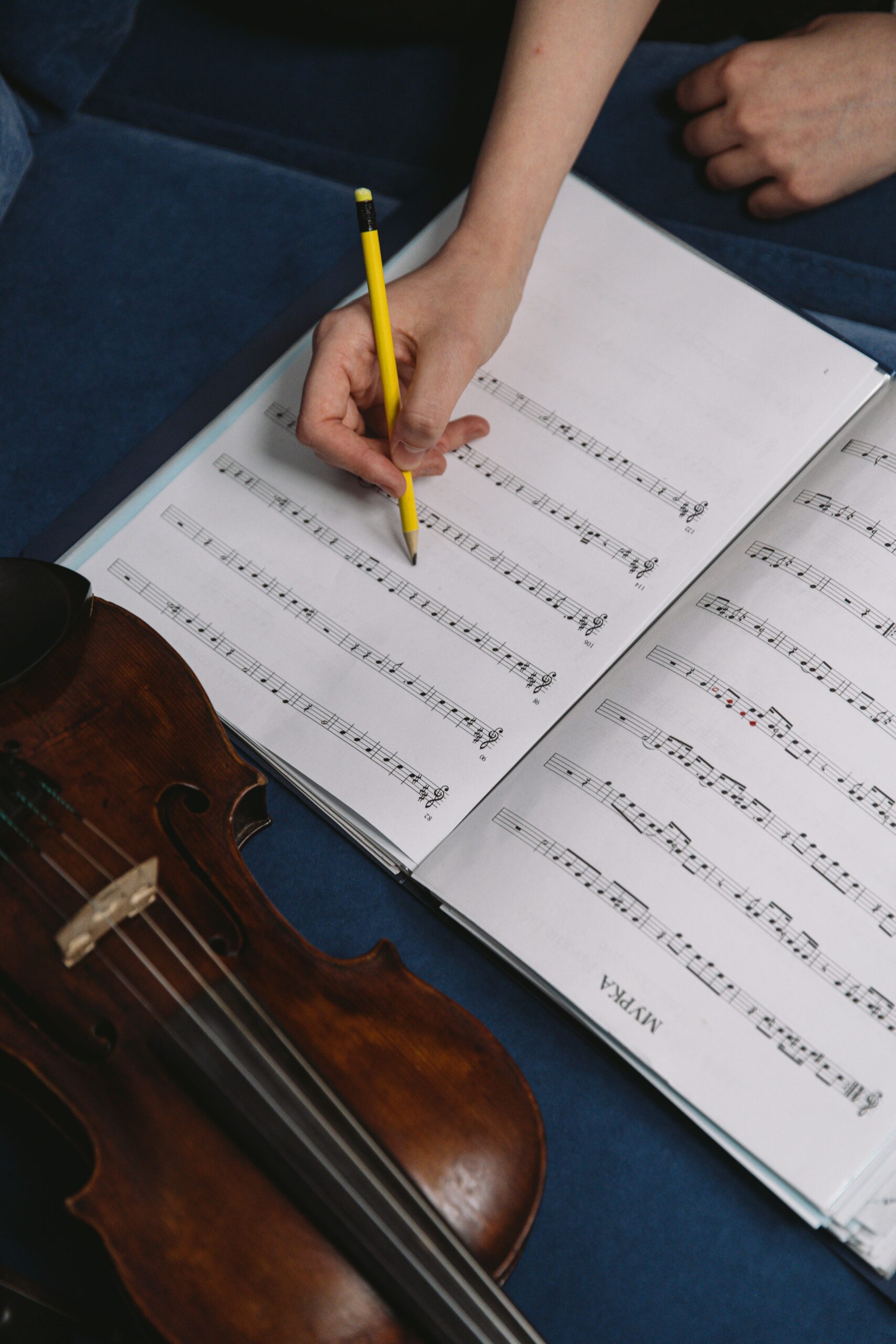 Close-up of a hand writing musical notes on sheet music with a violin beside it.